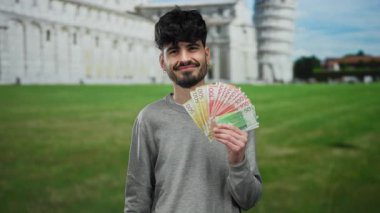 İtalya 'da pisa kulesinin önünde duran bir adam yeşil çimlere ve antik mimariye karşı kendine güvenen bir ifadeyle renkli Norveç banknotları tutuyor..
