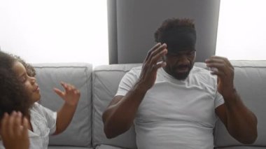 Babası kulaklarını kapatırken kızı da rahat bir oturma odasındaki koltukta onunla konuşuyor. Aile etkileşimlerini gösteriyor ve evde şakacı bir bağ kuruyor..