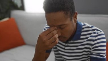 Oturma odasındaki koltukta oturan genç adam, modern bir dairedeki stres ve tefekküre işaret ediyor..