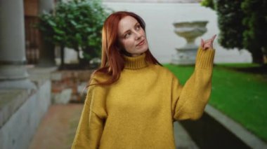 Sarı kazaklı, kızıl saçlı kadın şehir caddesinde, açık havada canlı, yemyeşil bir sahne sergiliyor..