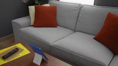 Rahat bir oturma odasında gri kanepeli ve turuncu yastıklı tablet kullanan bir kadın rahat bir atmosfer yaratıyor..