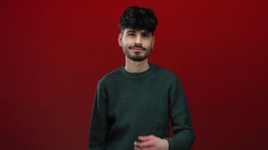 Canlı kırmızı bir arka planda gülümseyen genç adam, neşeli bir şekilde uzanıyor, arkadaşlığı, nişanı ve sıcaklığı modern, izole edilmiş bir portre ortamında aktarıyor..