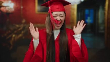 Kırmızı mezuniyet elbisesi içindeki genç kadın kapalı bir müze ortamında sevinçle kutlama yapıyor. Zarif dekorlarla çevrili mutluluk ve başarıyı ifade ediyor..