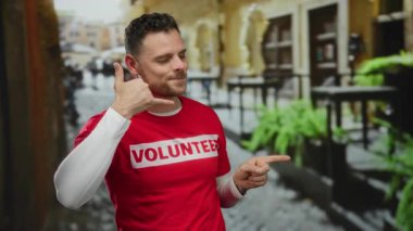 Şehir sokağında kırmızı gönüllü tişörtü giymiş, açık havada mutlu görünen bir adam var..