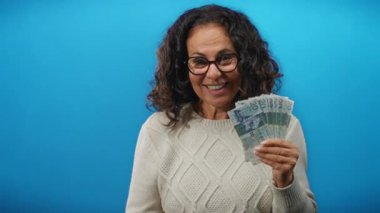 Hong Kong dolarıyla kutlayan bir kadın mavi arka planda heyecan ve neşe sergiliyor..