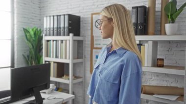 Kitaplıklar ve modern dekorlarla çevrili, kolları çapraz bir ofiste duran bir kadın profesyonel ve kendine güvenen bir çalışma ortamı sergiliyor..