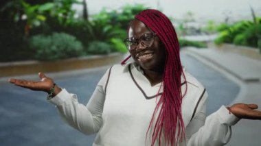 Şehir caddesinde kolları açık gülümseyen gözlüklü ve örgülü bir kadın, şehir tarzı ve açık hava ifadesi sergiliyor..