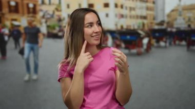 Pembe gömlekli sarışın kadın, hayat dolu bir şehir sokağında regl bardağını inceliyor, arka planda yürüyen insanlar, açık havada sağlık bilincini vurguluyor..