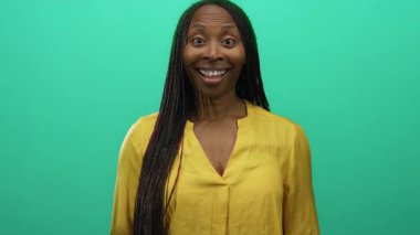 Canlı yeşil bir arkaplan önünde mutlu bir şekilde gülümseyen kadın, sarı bir gömlek giyiyor, pozitiflik ve sıcaklık yayıyor, sade bir arkaplanda izole edilmiş.