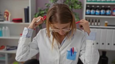 Steteskoplu, beyaz önlüklü kadın doktor klinikte gülümsüyor. Tıbbi ekipman ve dosyalar raflarda görünüyor..