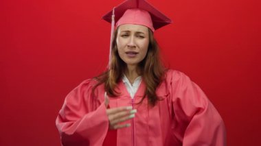 Pembe mezuniyet şapkası ve cüppeli genç bir kadın hapşırıyor, canlı kırmızı bir arkaplan üzerine kurulmuş, yeni mezun olmuş birinin komik anını yakalıyor..