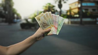 Bir şehir caddesinde Norveç kronu banknotları tutuyor, şehir yaşamını ve finans temalarını açık hava ortamında yakalıyor..