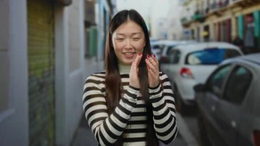 Arka planda arabaları olan bir kadın, çizgili süveter giyiyor, şehirde neşeli bir ifade sergiliyor, güzelliği ve gençliği dış mekandaki cazibeyle somutlaştırıyor..