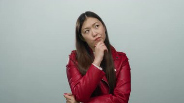 Beyaz bir arkaplan üzerinde düşünceli bir kadın, uzun siyah saçlı kırmızı bir ceket giyiyor, tefekkür ve ifade sergiliyor.