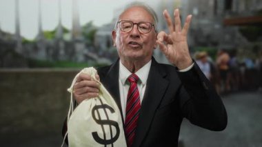 Takım elbiseli kıdemli adam, antik Roma harabelerinde para çantası taşıdığını gösteriyor. Açık havada yapılan iş ilişkilerinde yolsuzluk olduğunu ima ediyor..