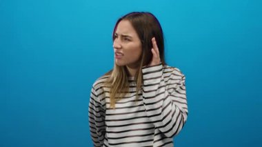 Mavi arka planda çizgili gömlek giyen kadın karışık bir ifade sergiliyor. Belirsizlik ve merak taşıyor. Sarışın kadın kulaklarına yakın ellerle izole edilmiş..