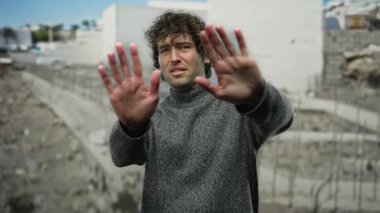 Şehir inşaatında elleri açık, kıvırcık jestleri olan genç bir adam şehir ortamında gri bir kazak giyiyor..