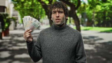 Czech Koruna 'yı elinde tutan İspanyol bir adam şehir sokaklarında finansman sağlıyor. Arka planda ağaçlarla finansal düşüncelere dalmış..