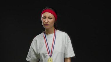 Madalya takan kadın, siyah arka plana karşı kaşlarını çatarak kırmızı saç bandı ve beyaz gömlekle kafa karışıklığını ifade ediyor, izole edilmiş stüdyo resmi, yüz ifadesini ve duygularını vurguluyor.