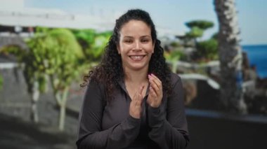 Arka planda palmiye ağaçları ve okyanusla güneşli bir sahilde el çırpan ve gülümseyen bir kadın..