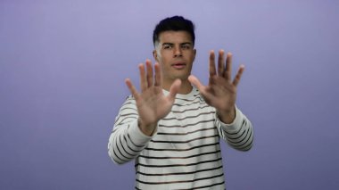 Genç adam mor bir arkaplan karşısında el kol hareketi yapıyor. Alkışlamaktan yüzünü kaplamaya kadar farklı ifadeler sergiliyor. Çizgili bir gömlek giyiyor, çeşitli duygular gösteriyor..