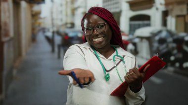 Afrika kökenli Amerikalı bir kadın steteskop ve panoyla şehrin işlek sokaklarında gülümsüyor..