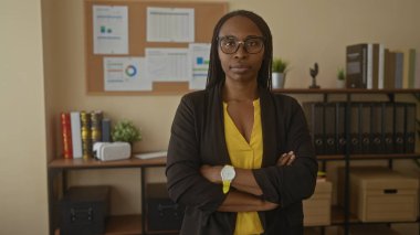 Ofiste kendine güvenen bir kadın, iş ortamını gösteren ciltler ve kitaplarla dolu bir kitaplığın önünde duran spor ceketi ayarlıyor.