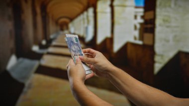 Güney Afrika Rand banknotlarını elinde tutan adam, şehir merkezinde döviz alışverişini vurguluyor. Güneş ışığı binanın ön cephesine gölge düşürüyor..