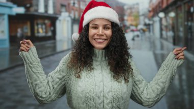 Dışarıda Noel Baba şapkası ve süveteri giyen bir kadın, ıslak caddede dikiliyor, kenar mahallelerde İspanyol kültürünü temsil eden, bayram sezonunda eğlencesini dile getiriyor..