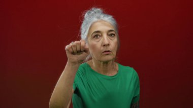 Kıdemli gri saçlı kadın kırmızı duvara vuruyor, ıssız bir yerde..