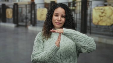 Şehir ortamında kıvırcık saçlı ve yeşil kazaklı bir kadın şehir manzarasının ortasında düşünceli bir ifade sergiliyor..