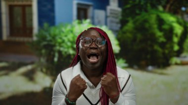 Parkta canlı örgüleri olan, gözlük takan ve rahat doğal ortamında heyecanını ifade eden bir kadın..