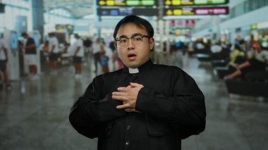 Dolu bir havaalanı terminalinde gezginlerle çevrili, parlak havaalanı tabelası altında endişeli bir ifade sergileyen Çinli bir rahip seyahat endişesi ve kültürel varlığı iletiyor..