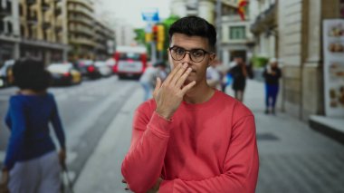 Kentsel caddede gözlüklü genç bir İspanyol gün ortasında kırmızı eşofman üstü giyiyordu. Düşünceli bir ifadeyle şehir hayatının meşguliyetini ima ediyordu..