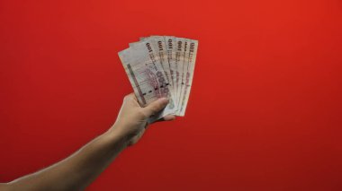 Suudi riyal banknotlarını izole edilmiş kırmızı zemin üzerinde tutan, Suudi Arabistan 'dan para gösteren, finans ve ekonomik kavramları vurgulayan bir adam.