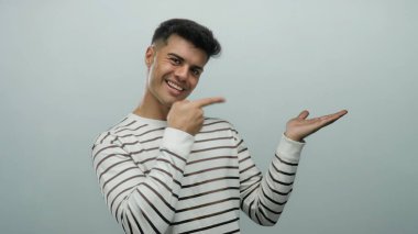 İzole edilmiş beyaz arka planda gülümserken çizgili gömlekli genç adam avucunu işaret ediyor.