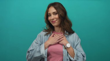 İzole edilmiş yeşil bir arka plana karşı kollarını açmış gülümseyen bir kadın günlük giysiler giyiyor. Portre tarzı bir ortamda dostluk ve mutluluk sergiliyor..