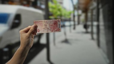 Kalabalık bir caddede elinde Türk lirası banknot tutan adam, açık havada para ve şehir yaşamını gözler önüne seriyor..