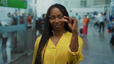 Sarı tişörtlü kıvırcık saçlı kadın havaalanı terminalinde küçük bir jest yapıyor..