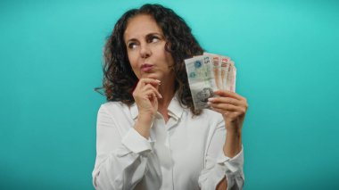 İngiliz banknotlarını tutan kadın mavi arka planda düşünceli bir ifadeyle