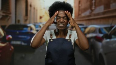 Yoğun şehir caddesinde, arka planda park halindeki arabalarla gün ışığında enerjik bir şekilde el kol hareketi yapan kadın..