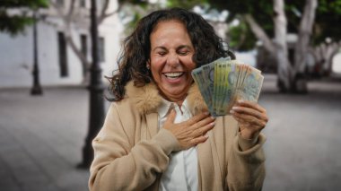 Bir şehir caddesinde neşeli bir ifadeyle neşe içinde Romanya banknotları tutan bir kadın, açık havada başarı ve mutluluk duygusunu somutlaştırıyor..
