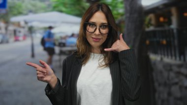 Genç bir kadın canlı şehir merkezindeki sokak kafesi terasına işaret ederken çağrı işareti yapıyor..