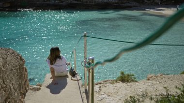 Mallorca 'daki Cala Llombards plajında turkuaz denizde dinlenen, çarpıcı Akdeniz manzarasına bakan, parlak güneş ışığı altında huzurlu tatil anlarının tadını çıkaran bir kadın..