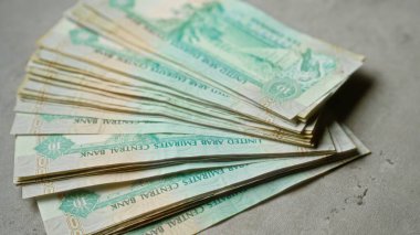 Bir yığın birleşik Arap Emirlikleri Dirham banknotları beton bir yüzeye yayılmış, para birimi detaylarını vurguluyor.