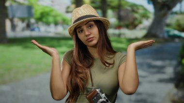 Parkta silkelenen, hasır şapka takan ve güneşli açık havada elinde antika kamera tutan bir kadın..