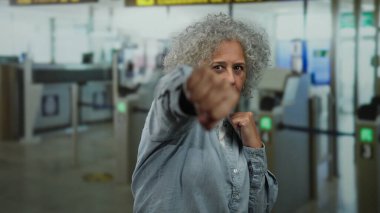 Gri saçlı kadın havaalanı terminalinde boks antrenmanı yapıyor. Seyahat ortamında azim ve zindeliğin ilginç bir karışımını yapıyor..