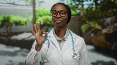 Kadın doktor dışarıda gözlük takıyor ve steteskoplu beyaz önlüklü normal bir jest yapıyor.