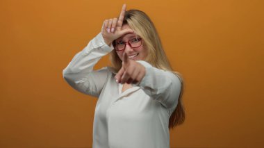 Ezik işareti yapan ve turuncu arka planda kameraya bakan bir kadın..