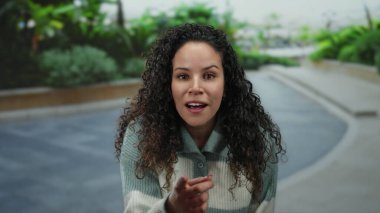 Kıvırcık saçlı genç bir İspanyol kadın sokakta kameraya bakıyor. Etrafı yemyeşil, neşeli bir ifadeyle çevrili. Neşeli, samimi bir anın altını çiziyor..